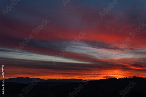 Gentle, beautiful orange and black summer sunset outdoors, in the mountains, with black silhouettes of trees © Bohdan