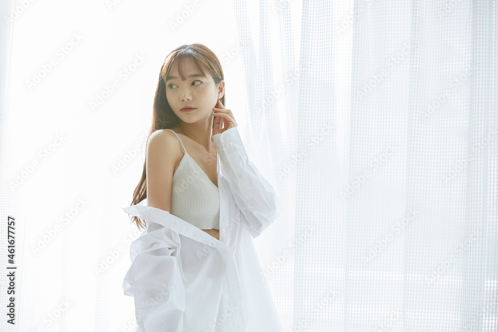 窓辺に立つ若い女性のナチュラルなビューティーポートレート