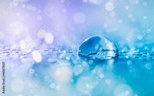 Transparent water drop on defocused background in violet and blue tones with bokeh and copy space in macro.