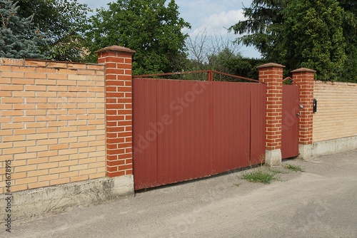 red metal gate and closed door on the wall of the brown brick fence on the street