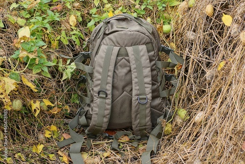 one big green tactical backpack stand on dry gray vegetation with leaves in nature