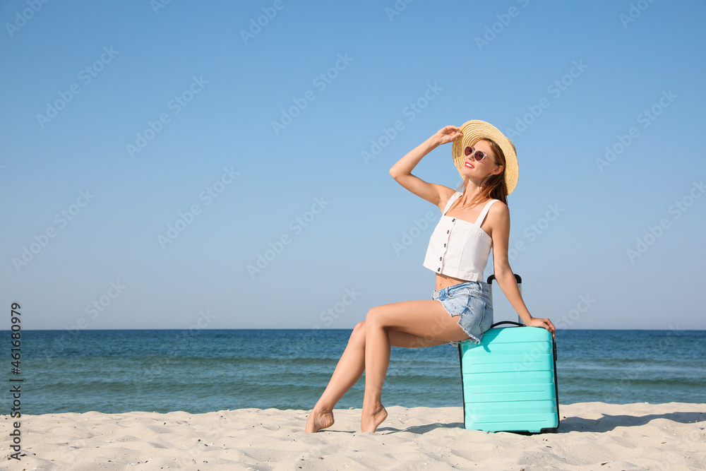 Beautiful woman with suitcase on sandy beach near sea