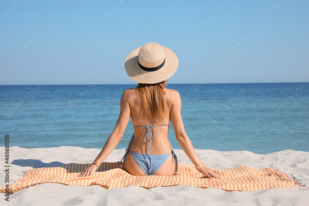 Woman sitting on beach towel near sea, back view