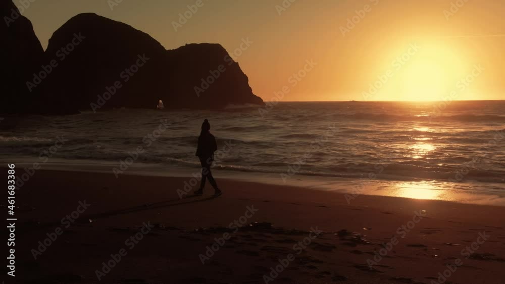 Aerial: Woman walking along the beach at sunset. Mendocino Coastline, California, USA Aerial: Woman walking along the beach at sunset. Mendocino Coastline, California, USA