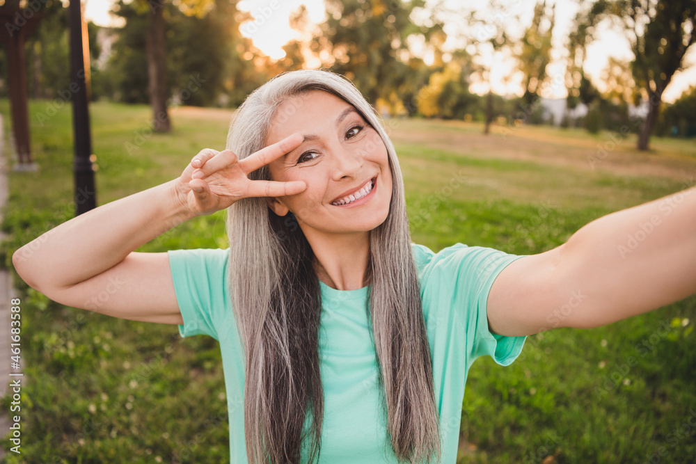 Self-portrait of attractive cheerful grey-haired woman showing v-sign having fun good mood rest relax fresh air wood outdoors Self-portrait of attractive cheerful grey-haired woman showing v-sign having fun good mood rest relax fresh air wood outdoors