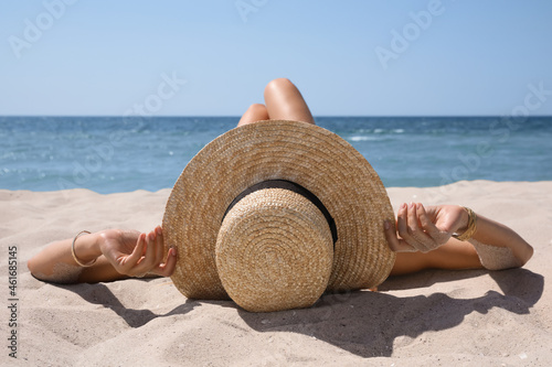 Woman with straw hat lying on sandy beach near sea photo