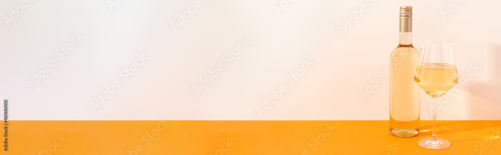 Bottle and glass of white wine on begie and orange background with deep shadows. Mock up drink with place for you lable and text