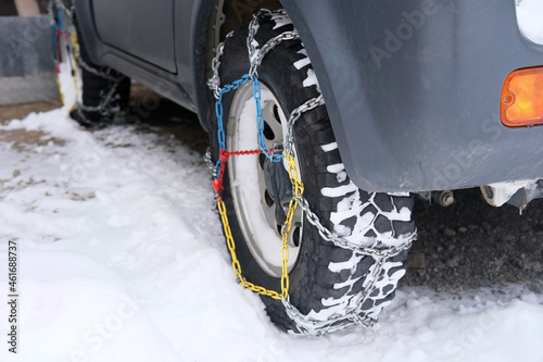 close-up wheel of a gray car in colored iron chains on the snow, winter travel safety concept with snow chains on tire