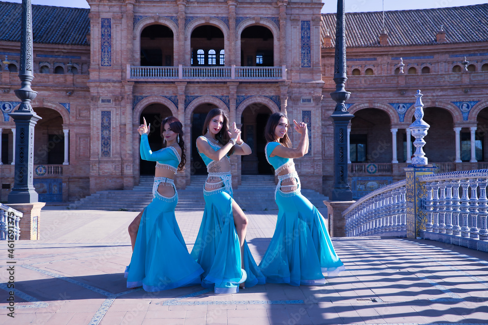 Three middle-aged Hispanic women, wearing turquoise costumes and rhinestones, to belly dance, simulating as if they had guns in their hands. Belly dance concept.
