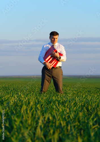 businessman holds an office red folder with documents in a green grass field - business concept