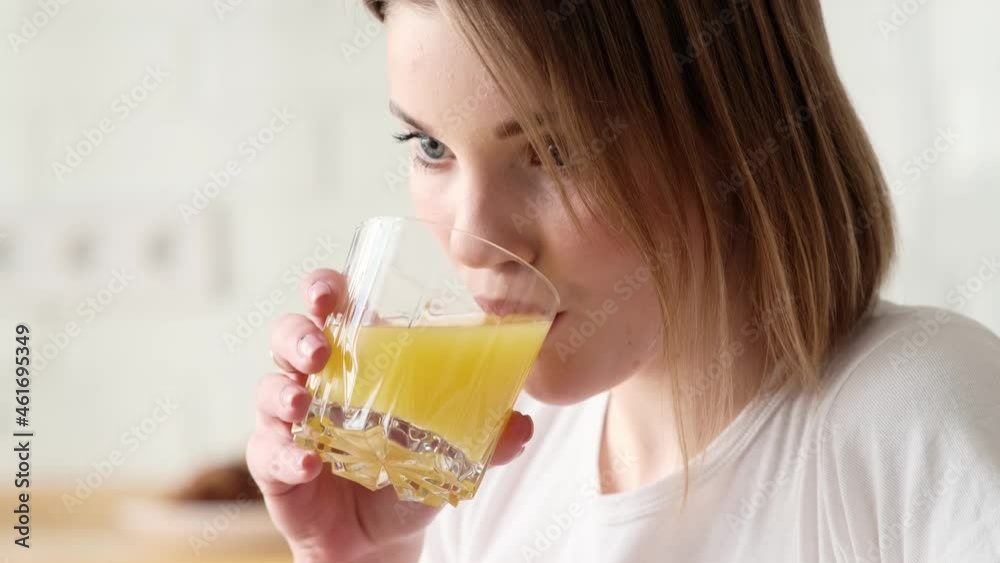 A pleased woman is using her laptop computer while drinking orange juice sitting inside the apartments A pleased woman is using her laptop computer while drinking orange juice sitting inside the apartments