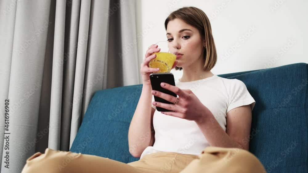 An attractive woman is using her smartphone while sitting on the sofa inside the apartments An attractive woman is using her smartphone while sitting on the sofa inside the apartments