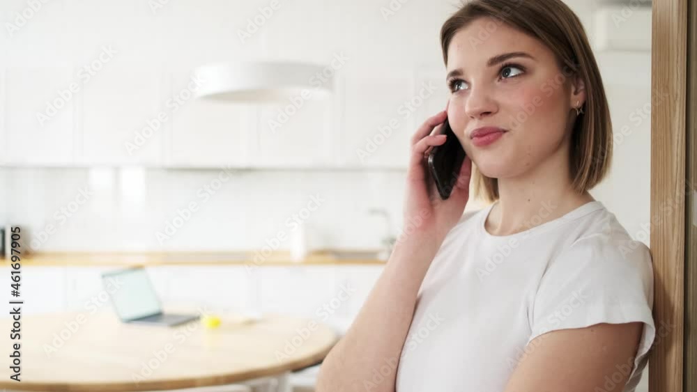 A pleased woman is talking on her smartphone while standing inside the apartments A pleased woman is talking on her smartphone while standing inside the apartments
