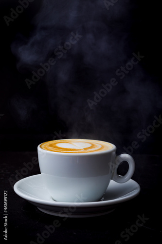 Cappuccino with steam and heart love latte art in white cup on the black table