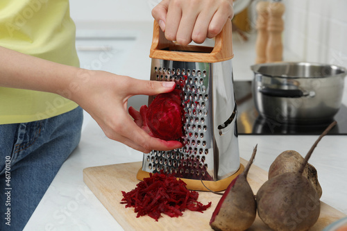 Woman grating fresh beetroot at kitchen counter, closeup