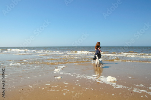 Young girl playing with a white dog on. Cromer beach in a sunny day of summer, joy, happiness, holiday, vacation in England, United Kingdom, Norfolk coast, North sea
