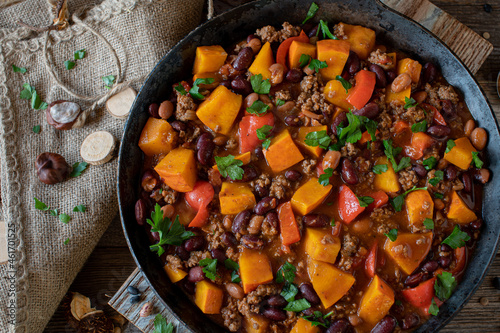 Stew with pumpkin, ground beef, kidney beans and vegetable in rustic cast iron skillet. Delicious meal for autumn and winter season