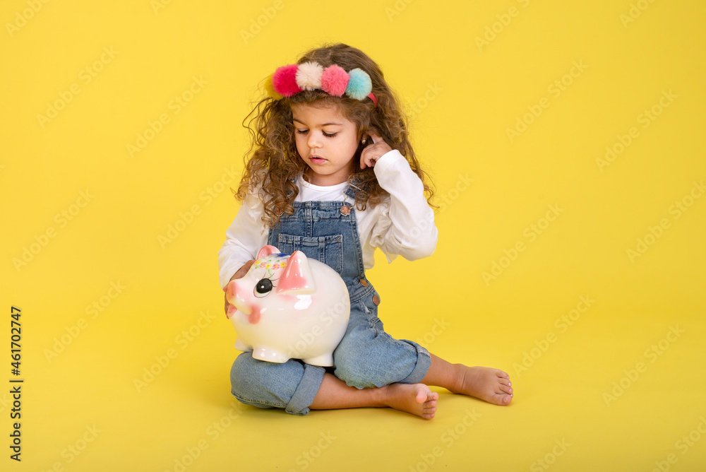 Happy  Little Children girl  saved a little money for future need wearing white T-shirt holding piggy bank, Saving money since childhood on yellow background  studio shot with copy space