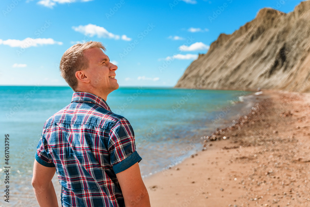 A young man in a shirt walks on an empty beach on Cape Chameleon in Crimea