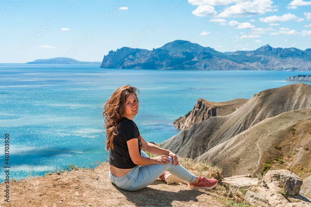 A young beautiful woman is sitting on a high mountain overlooking the coast with hills and mountains, the concept of traveling and climbing in the mountains