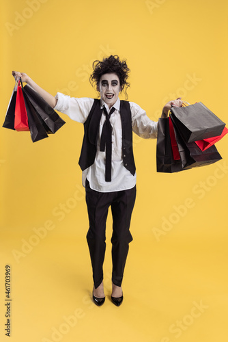 Portrait of excited woman in Halloween costume holding bunck of shopping bags isolated over yellow background. Black Friday sales photo