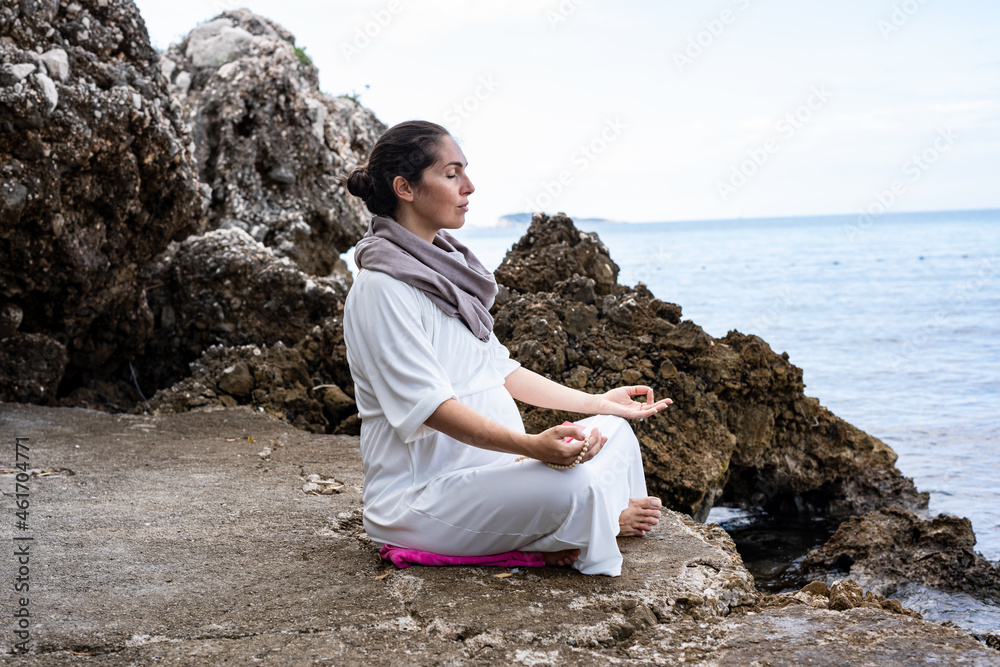 Beautiful pregnant woman is meditating on the beach	