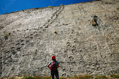 A girl tourist in a red helmet looks at the fossil footprints of ancient reptiles on a rock in the dinosaur park in Sucre, Bolivia photo