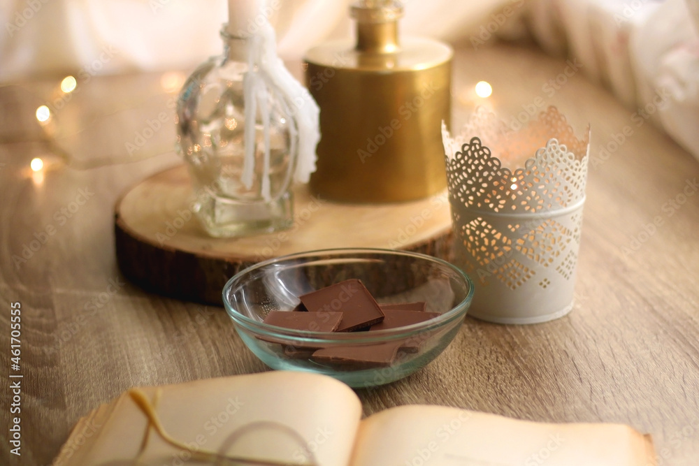 Bowl of chocolate, book, reading glasses, candles and vase with flowers on the table. Selective focus. Bowl of chocolate, book, reading glasses, candles and vase with flowers on the table. Selective focus.