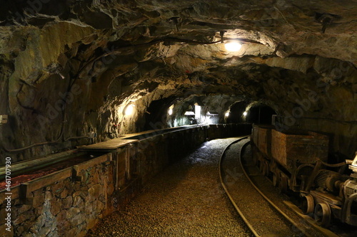 Antique and rusted interior of an old copper mine including dark tunnels, tungsten light, railroad track, rusty wagons, broken wheels and other mining equipment