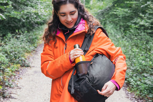 A woman picking up a metal bottle from her backpack. Adventure concept. Trekking concept. Copy space.
