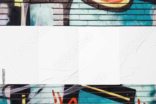 Closeup of colorful messy painted urban wall texture with four wrinkled glued poster templates. Modern mockup for design presentation with clipping path. Creative urban city background. 