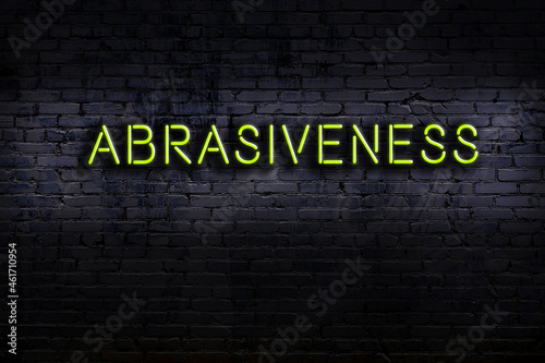 Neon sign. Word abrasiveness against brick wall. Night view