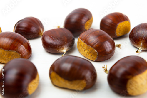 Ripe chestnuts, freshly picked and removed from the hedgehog, arranged on a white wooden surface.