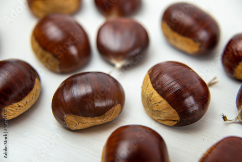 Ripe chestnuts, freshly picked and removed from the hedgehog, arranged on a white wooden surface.