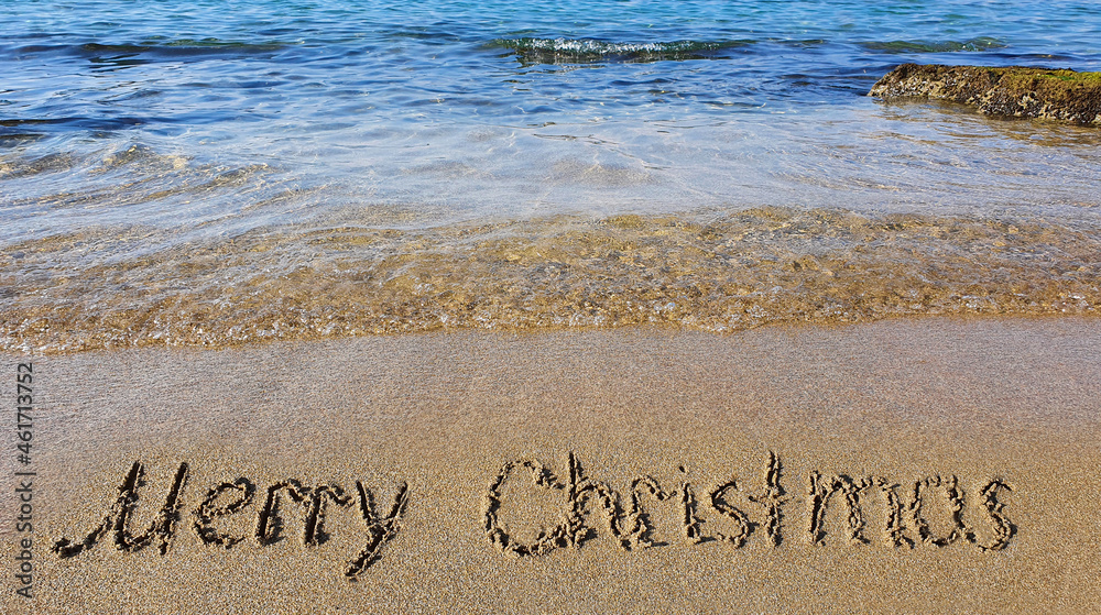 Fototapeta premium Word Merry Christmas written on the sand near the sea.