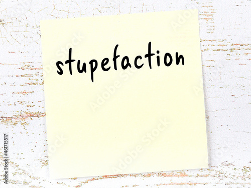 Yellow sticky note on wooden wall with handwritten word stupefaction