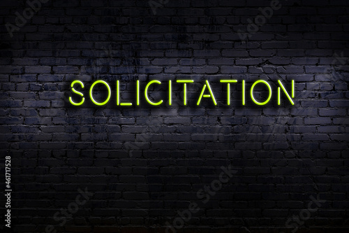 Night view of neon sign on brick wall with inscription solicitation photo