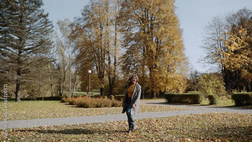 Plump happy woman in mustard turtleneck, coat and jeans is spinning joyfully in autumn sunny park. Beautiful general plan of autumn nature. Young woman smiles, pulls her hand towards camera. Plump happy woman in mustard turtleneck, coat and jeans is spinning joyfully in autumn sunny park. Beautiful general plan of autumn nature. Young woman smiles, pulls her hand towards camera.