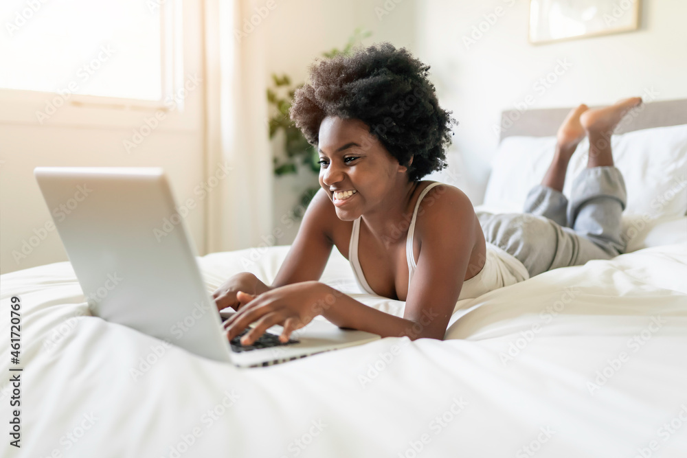 young black woman using a laptop in bright bedroom young black woman using a laptop in bright bedroom