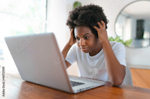 young African female entrepreneur working online with a laptop while sitting at her kitchen table at home look sad