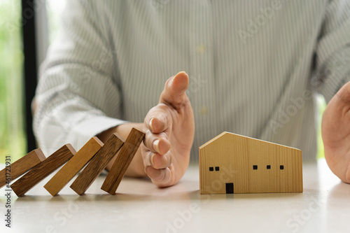 A businessman protects the house from falling wooden dominoes. of wooden blocks, home insurance concepts for the stability and safety of the property