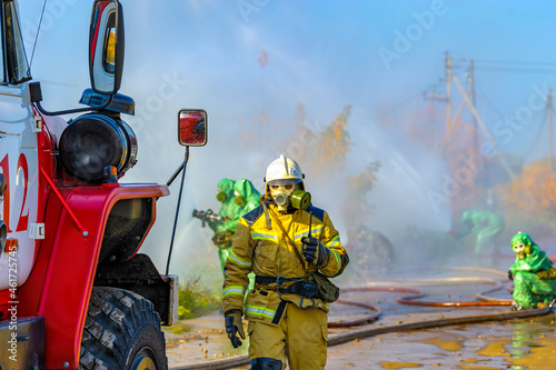 Rescuers in chemical protection suits eliminate an ammonia leak and extinguish a fire at a chemical plant. Rescue operation to create water barriers to toxic chemical cloud after the accident.