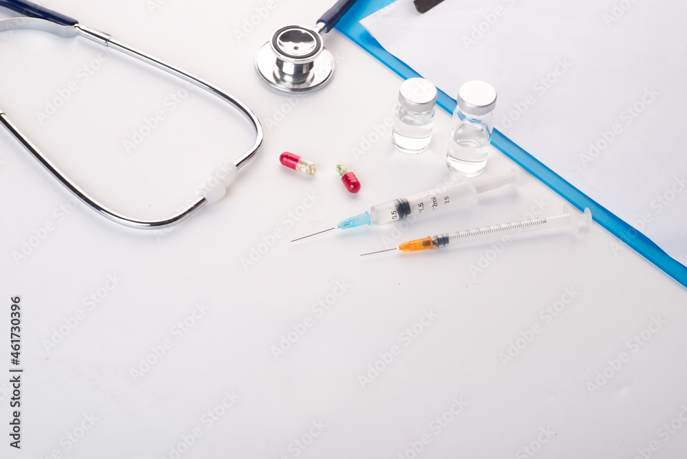 Pills spilling out of pill bottle syringe thermometer and stethoscope on white background