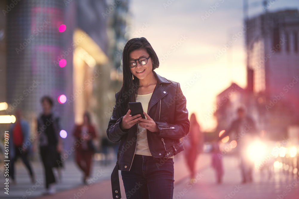 Fototapeta premium Beautiful young Asian woman walking outside in a modern city, using an application in her phone