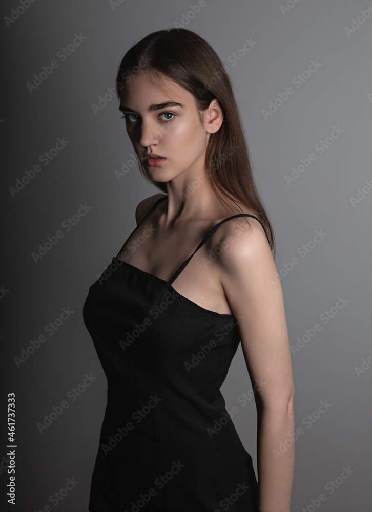 Beautiful woman with nude makeup and volume brown long hair looking mystery in black dress on grey background. Closeup. Art Beautiful woman with nude makeup and volume brown long hair looking mystery in black dress on grey background. Closeup. Art
