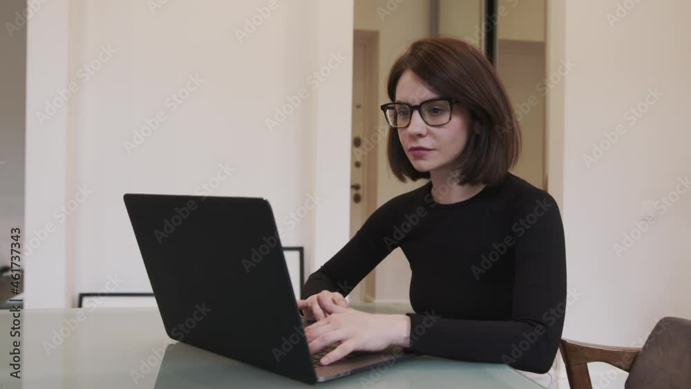 Smiling woman sitting, using laptop in office room. Elegant manager in black sweater. Freelancer typing on a device indoors, gimbal shot. Concept of remote work Smiling woman sitting, using laptop in office room. Elegant manager in black sweater. Freelancer typing on a device indoors, gimbal shot. Concept of remote work