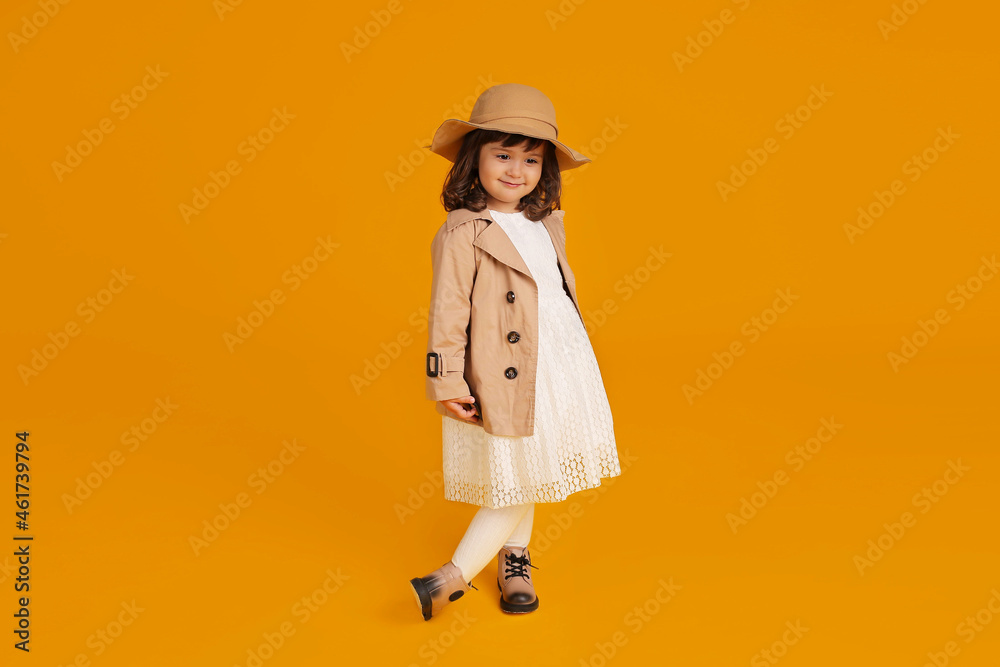 a little beautiful girl in a white dress beige raincoat and beige hat beige shoes on a yellow background a little beautiful girl in a white dress beige raincoat and beige hat beige shoes on a yellow background