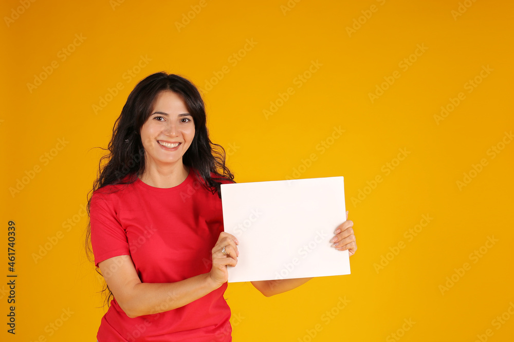 beautiful happy brunette girl with long hair in a red T-shirt holding a white sheet of paper yellow background beautiful happy brunette girl with long hair in a red T-shirt holding a white sheet of paper yellow background