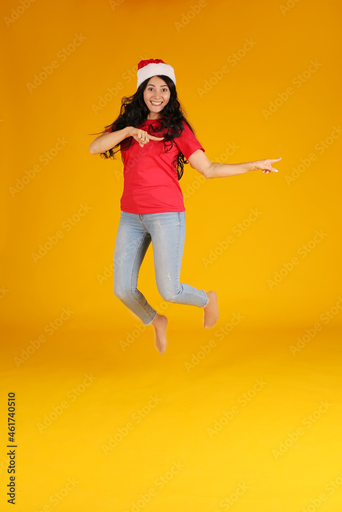 beautiful happy brunette girl with long hair in santa claus hat jumping new year concept yellow background