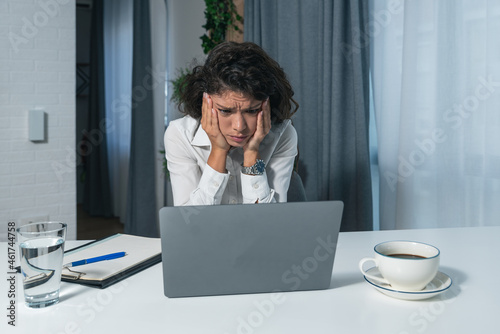 Young successful business woman sitting in an office and works on a laptop unable to work due to loud noise coming from the upstairs office where renovations are underway and workers are making noise photo